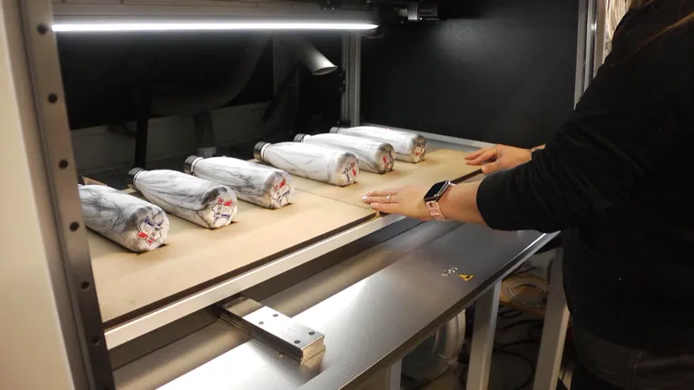 User loading marble-style bottles into Trotec SpeedMarker laser marking machine