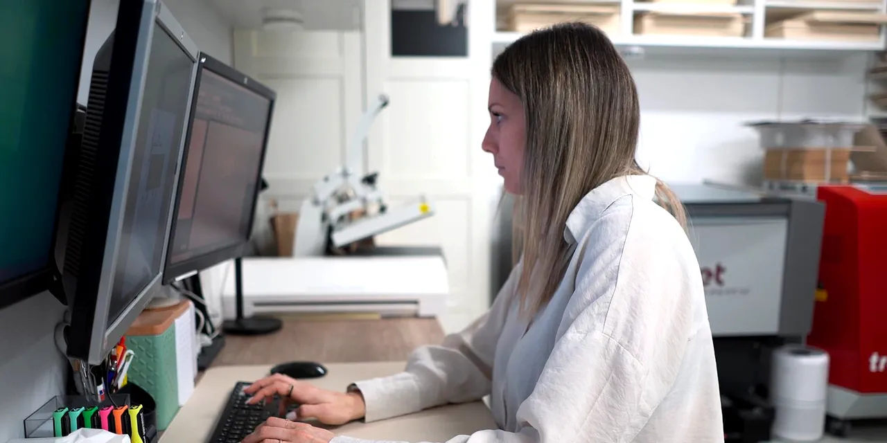 Designer using dual monitors with Trotec Speedy laser cutter and Ruby software in background