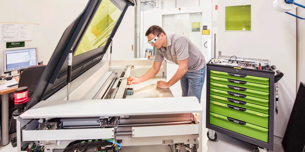 Technician calibrating Trotec Speedy series CO₂ laser cutter in modern workshop