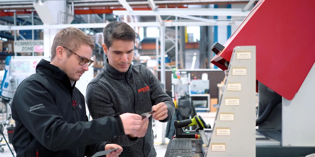 Technicians inspecting engraved metal plate beside Trotec SpeedMarker laser marking machine