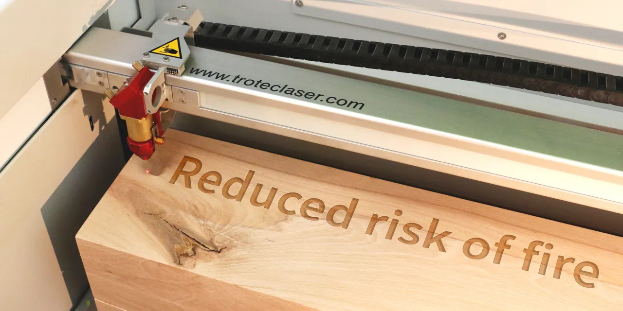 Trotec CO₂ laser engraving machine etching 'Reduced risk of fire' on wooden block